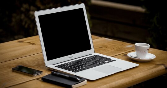 Laptop mit Tasse, Block, Stift und Handy