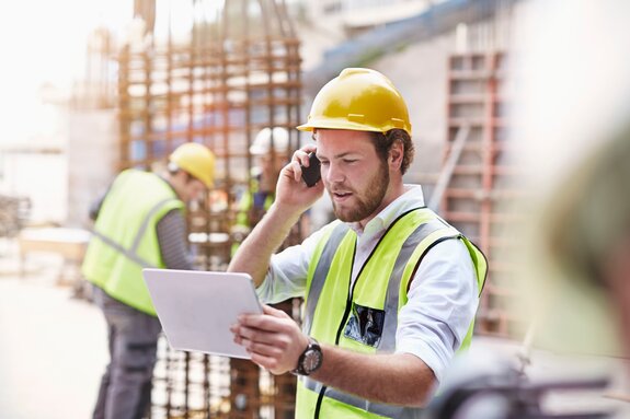 Engineer digital tablet talking on cell phone at construction site