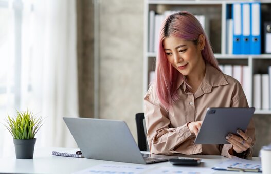 Portrait of a young Asian businesswoman working on a tablet with a laptop at the thinking office. analyze marketing data online business ideas.
