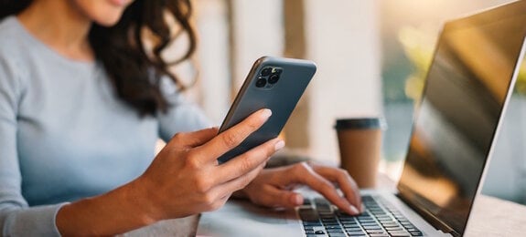 Woman using smartphone and working at laptop computer.