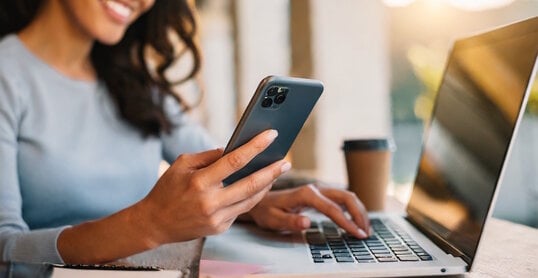 Woman using smartphone and working at laptop computer.