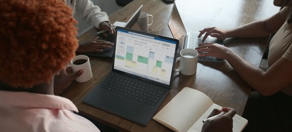 Drei Personen in einer Besprechung an einem Tisch besprechen den Zeitplan auf ihrem Microsoft-Laptop