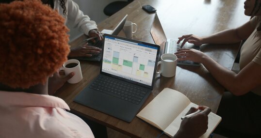 Drei Personen in einer Besprechung an einem Tisch besprechen den Zeitplan auf ihrem Microsoft-Laptop