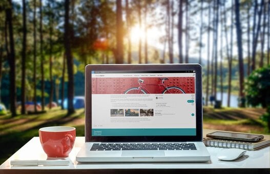 Laptop mit Valo Intranet Seite und mit roter Tasse vor einem Wald.