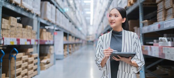 Portrait of asian woman business owner using digital tablet checking amount of stock product inventory on shelf at distribution warehouse factory