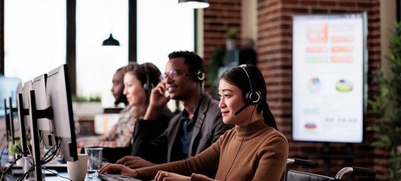 Paralyzed asian receptionist working at call center helpdesk in disability friendly office. Female operator wheelchair user with impairment giving assistance on customer service helpline