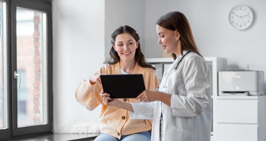 medicine, healthcare and people concept - female doctor with tablet pc computer talking to smiling woman patient at hospital