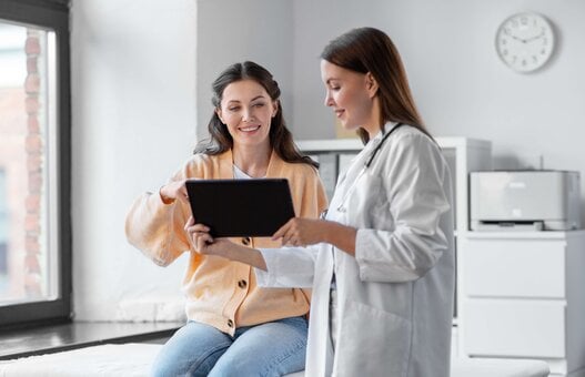 medicine, healthcare and people concept - female doctor with tablet pc computer talking to smiling woman patient at hospital