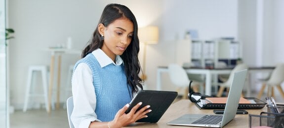 Trendy marketing professional using an online app to network, meet deadlines and stay connected during office hours. Young business woman using her laptop and tablet while working in the office.