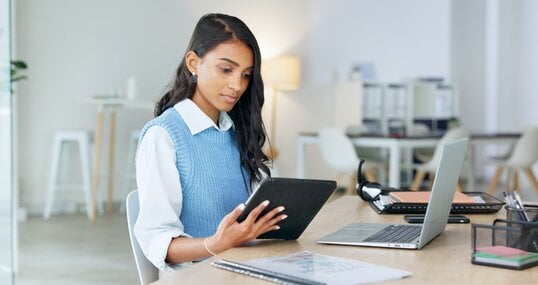 Trendy marketing professional using an online app to network, meet deadlines and stay connected during office hours. Young business woman using her laptop and tablet while working in the office.