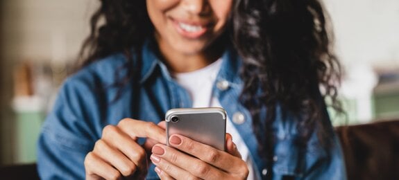 Cropped shot of an african-american young woman using smart phone at home. Smiling african american woman using smartphone at home, messaging or browsing social networks while relaxing on couch