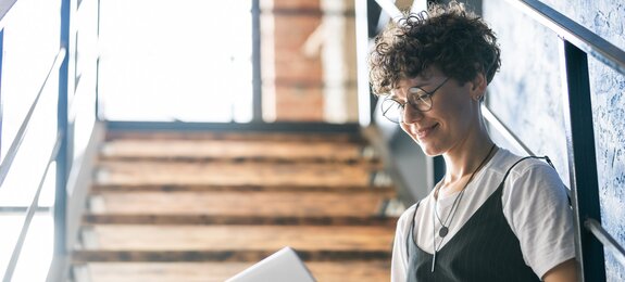 Pretty designer in casualwear sitting on staircase with laptop on her knees