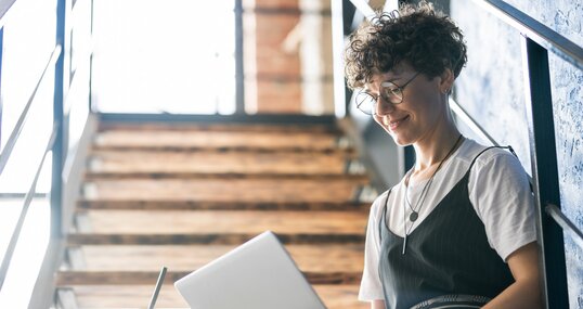 Pretty designer in casualwear sitting on staircase with laptop on her knees