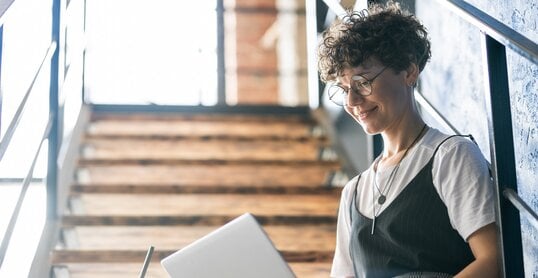 Pretty designer in casualwear sitting on staircase with laptop on her knees