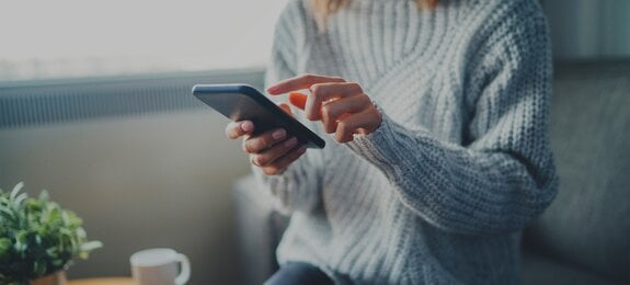 Closeup image of young hipster girl wearing knitted sweater using modern smaertphone device while chilling at home, communication and socail network concept, woman browsing the internet