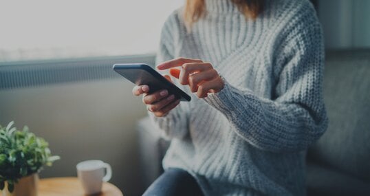 Closeup image of young hipster girl wearing knitted sweater using modern smaertphone device while chilling at home, communication and socail network concept, woman browsing the internet
