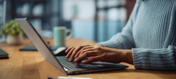 Close Up on Hands of a Female Specialist Working on Laptop Computer at Cozy Home Living Room while Sitting at a Table. Freelancer Woman Chatting Over the Internet on Social Networks.