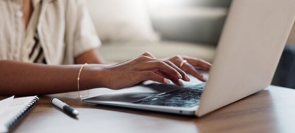 Desk, hands typing and laptop in home for remote work, internet search or blog. Closeup, computer and woman on keyboard at table in living room, writing email and communication on digital technology