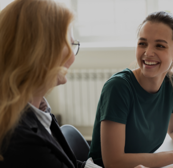 Pleasant workday. Two women colleagues employees of diverse age sharing points of view at workplace in office, happy smiling millennial female trainee discussing business ideas with adult aged trainer