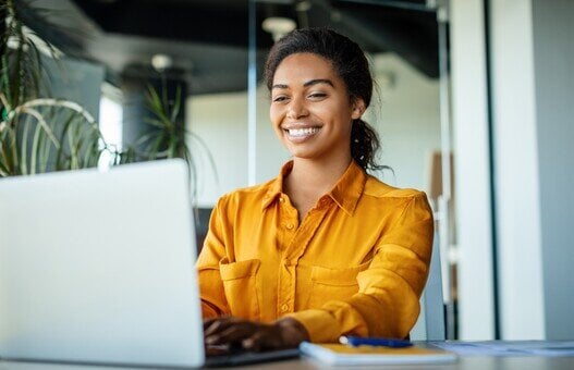 Happy black businesswoman using laptop typing and working online while sitting at workplace in office, copy space