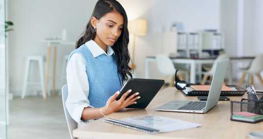 Trendy marketing professional using an online app to network, meet deadlines and stay connected during office hours. Young business woman using her laptop and tablet while working in the office