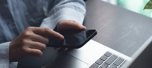 Closeup of woman finger touching on mobile phone screen. Asian woman using smartphone while sitting at table with laptop computer at home office, online shopping, mobile banking, internet payment