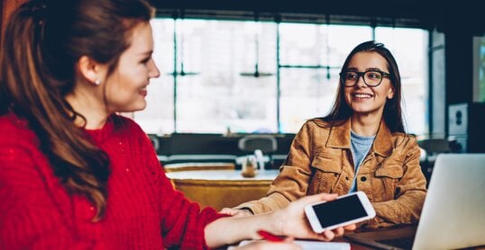 Two happy female friends enjoying positive conversation looking to each other in break of learning and searching information for test indoors, smiling hipster girls talking and spending time together