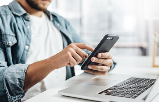 Young man with smartphone in his hands. Modern businessman at sunny office. Freelancer at work.