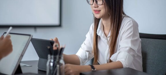 Junge Frau sitzt an Tisch und arbeitet mit Tablet