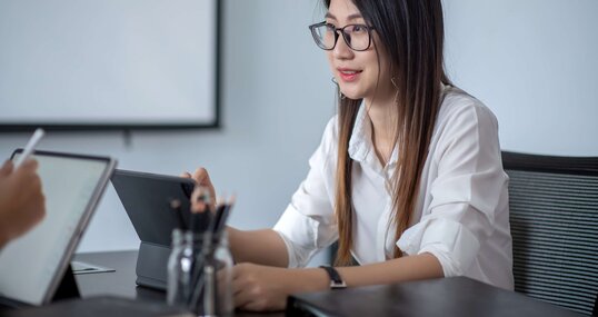 Junge Frau sitzt an Tisch und arbeitet mit Tablet