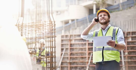 Ingenieur mit einem Tablet in der Hand telefoniert auf einer Baustelle