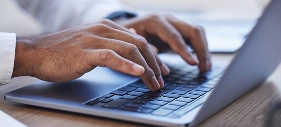 Laptop, office and hands typing at desk for online documents, writing email and business proposal. Technology, networking and zoom of businessman on computer for research, report and website review