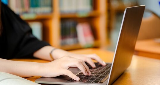 Female student using laptop on desk at library