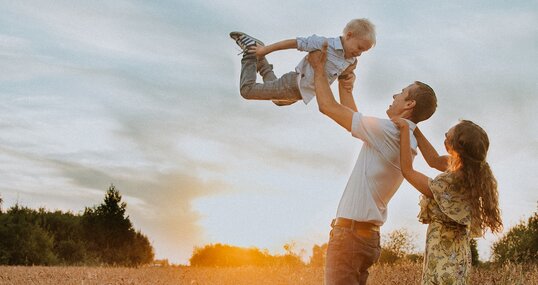 Fröhliche Familie mit Kind auf einem Feld beim Sonnenuntergrang